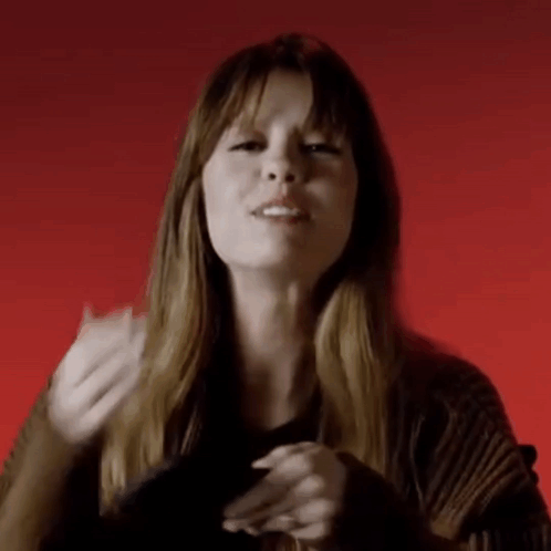 A Woman Is Making A Gesture With Her Hands In Front Of A Red Background While Wearing A Black Sweater . GIF