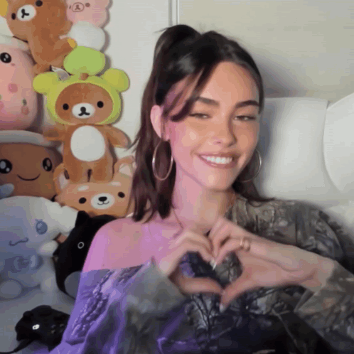 A Woman Is Making A Heart Shape With Her Hands In Front Of Stuffed Animals GIF