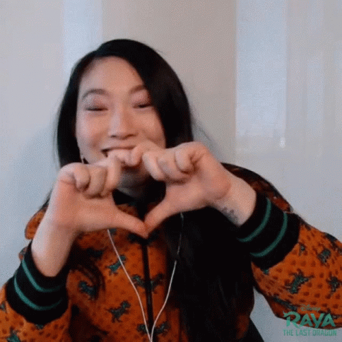 A Woman Is Making A Heart With Her Hands While Wearing Headphones . GIF