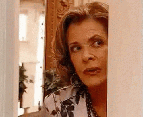 A Woman Is Peeking Out From Behind A Wall And Looking At The Camera . GIF