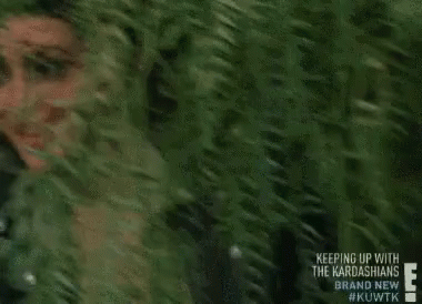 A Woman Is Peeking Out Of A Tree And Smiling . GIF