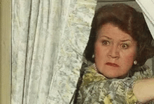 A Woman Is Peeking Out Of A Window With A Shocked Look On Her Face . GIF