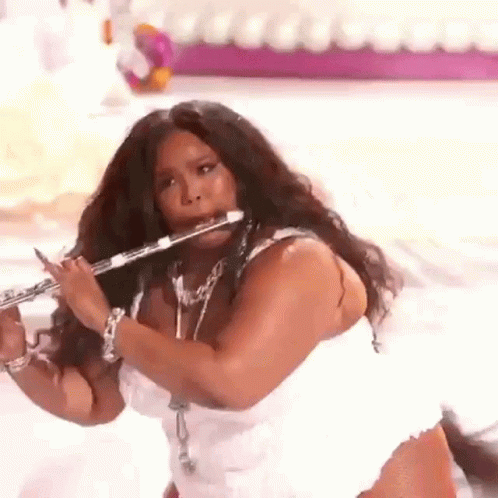 A Woman Is Playing A Flute On A Stage While Wearing A White Dress . GIF