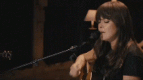 A Woman Is Playing A Guitar And Singing Into A Microphone GIF