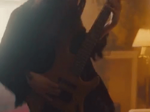 A Woman Is Playing A Guitar In A Dark Room While A Man Is Holding Her . GIF