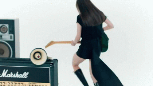 A Woman Is Playing A Guitar Next To A Marshall Amplifier . GIF