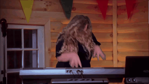 A Woman Is Playing A Keyboard In Front Of A Log Wall GIF