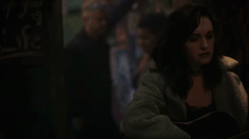 A Woman Is Playing An Acoustic Guitar In A Dark Room . GIF