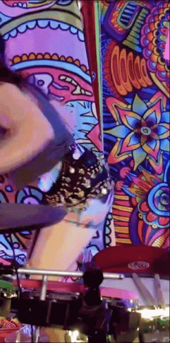 A Woman Is Playing Drums In Front Of A Colorful Wall Mural . GIF