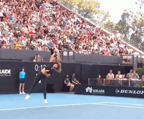 A Woman Is Playing Tennis In Front Of A Crowd And A Sign That Says Adelaide GIF