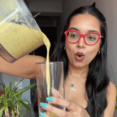 A Woman Is Pouring A Smoothie Into A Glass GIF