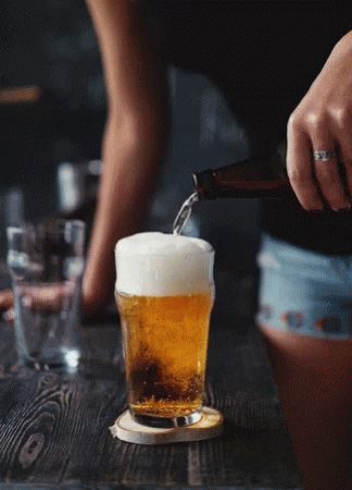A Woman Is Pouring Beer Into A Glass On A Table GIF