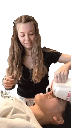 a woman is pouring milk into another woman 's face who is wearing a sweatshirt that says ' abercrombie '