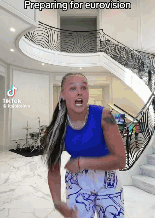 A Woman Is Preparing For Eurovision In Front Of A Spiral Staircase GIF