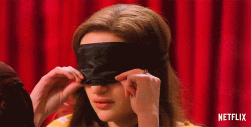 A Woman Is Putting On A Black Eye Mask On Her Face . GIF