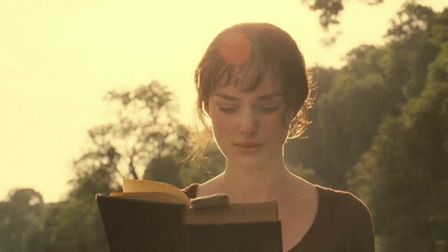 A Woman Is Reading A Book In Front Of A Forest GIF