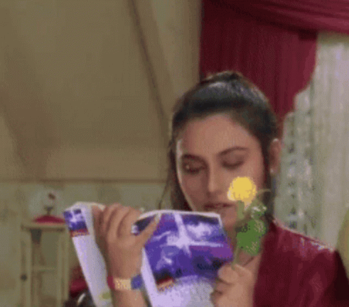 A Woman Is Reading A Book While Holding A Flower In Her Hand GIF