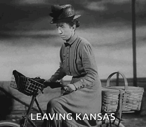 A Woman Is Riding A Bike With The Words Leaving Kansas Written On It GIF