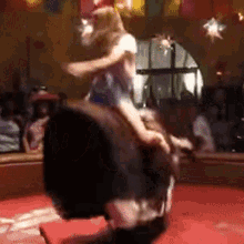 A Woman Is Riding On The Back Of A Bull In A Rodeo Arena . GIF
