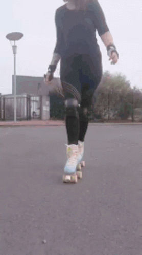 A Woman Is Rollerblading Down A Street With A Street Light In The Background . GIF