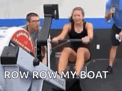A Woman Is Rowing A Boat In A Gym With A Man Standing Behind Her . GIF