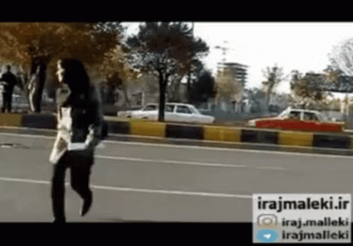 A Woman Is Running Down A Street With A Sign That Says Irajmaleki.ir GIF