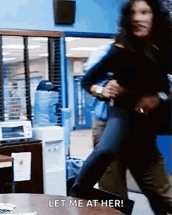 A Woman Is Running In A Room With The Words Let Me At Her Written On The Table . GIF