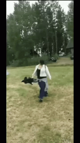 A Woman Is Running With A Black Dog In Her Arms In A Field GIF