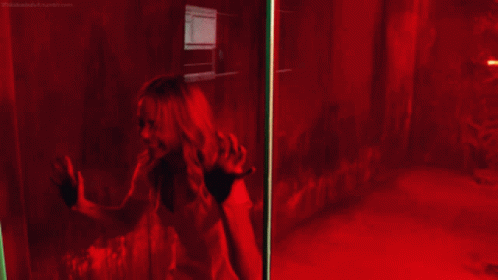 a woman is screaming behind a glass door with a red light behind her