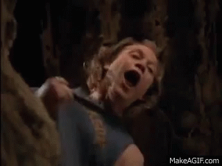 a woman is screaming in a cave with her mouth open while a man is holding her .