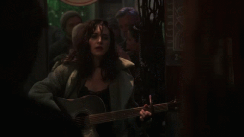 A Woman Is Singing And Playing A Guitar In Front Of A Sign That Says Tuesdays GIF