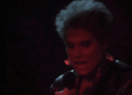 A Woman Is Singing Into A Microphone In A Dark Room With Red Lights Behind Her . GIF