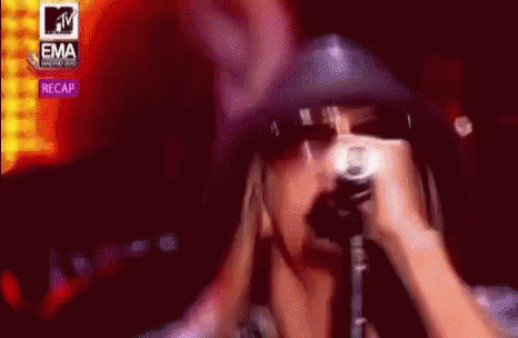 A Woman Is Singing Into A Microphone In Front Of A Mtv Logo . GIF