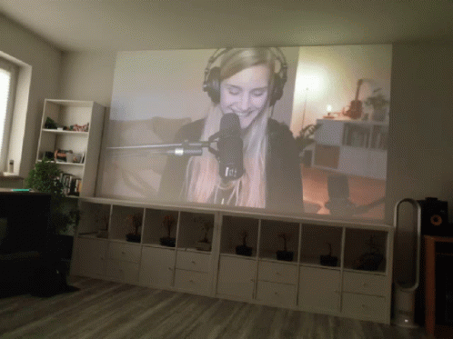 A Woman Is Singing Into A Microphone On A Large Screen GIF