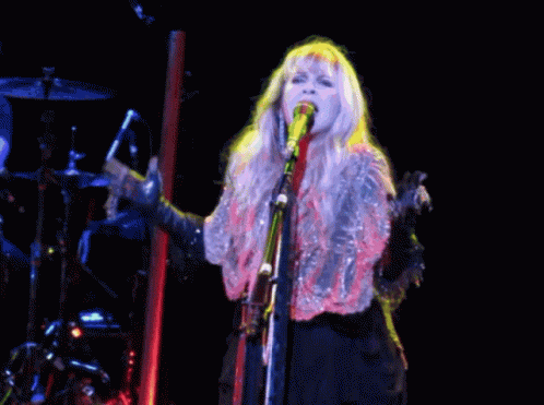 A Woman Is Singing Into A Microphone On A Stage GIF