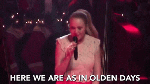A Woman Is Singing Into A Microphone On A Stage And The Words `` Here We Are As In Olden Days '' Are Behind Her . GIF