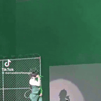 A Woman Is Singing Into A Microphone On A Stage While A Man Stands Behind Her . GIF