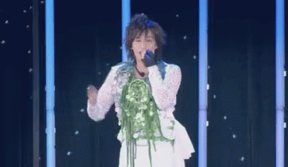 A Woman Is Singing Into A Microphone On A Stage With A Bouquet Of Flowers On Her Neck . GIF