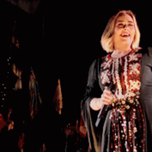 A Woman Is Singing Into A Microphone On Stage GIF