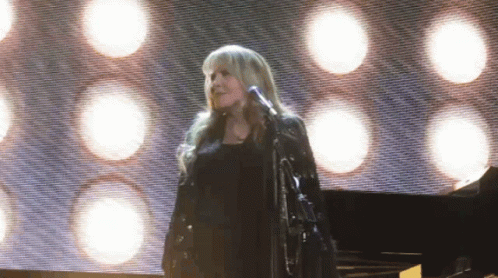 A Woman Is Singing Into A Microphone On Stage GIF
