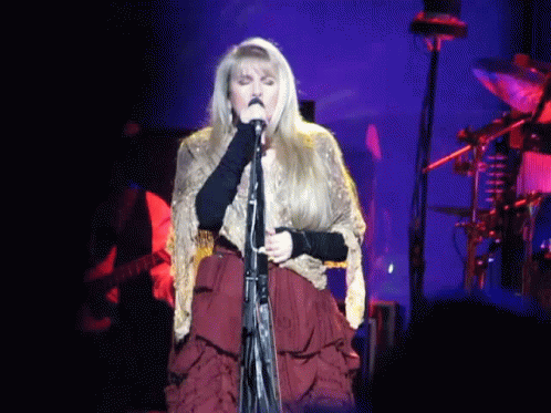 A Woman Is Singing Into A Microphone On Stage GIF