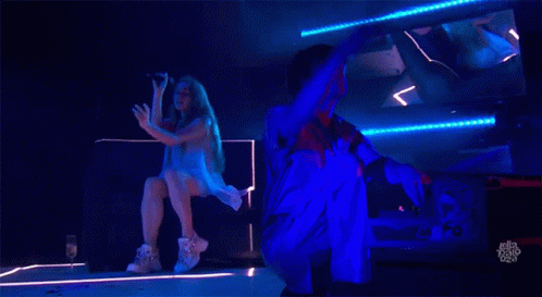 A Woman Is Singing Into A Microphone While A Man Is Kneeling Down Behind Her GIF