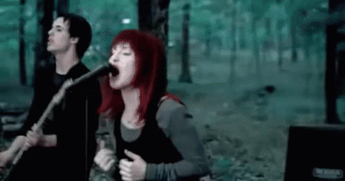 A Woman Is Singing Into A Microphone While A Man Plays A Guitar . GIF
