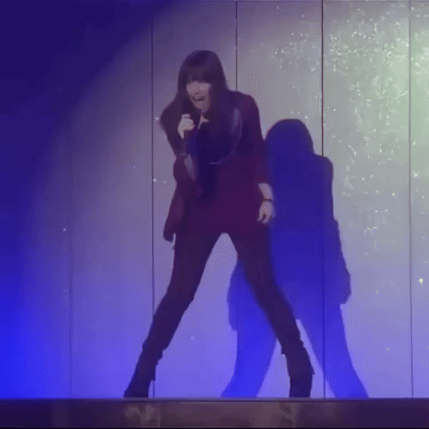 A Woman Is Singing Into A Microphone While Dancing On A Stage . GIF