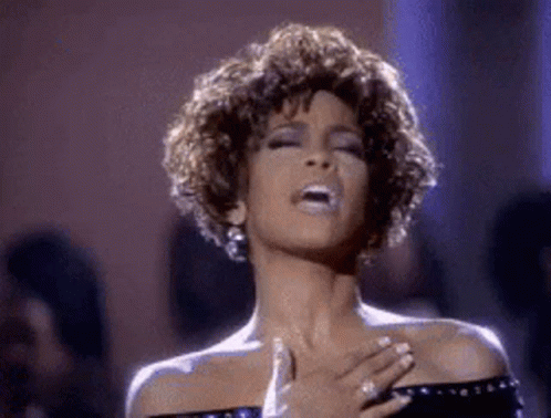 a woman is singing into a microphone while holding her hands to her chest .