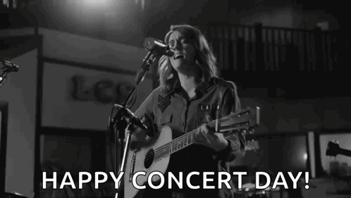 A Woman Is Singing Into A Microphone While Playing A Guitar On A Stage . GIF