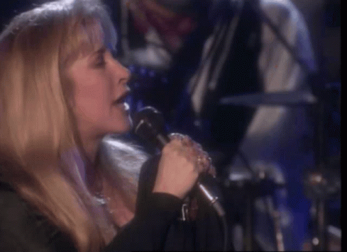 A Woman Is Singing Into A Microphone While Sitting On A Stage . GIF