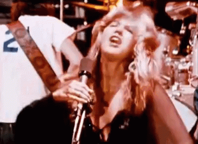 A Woman Is Singing Into A Microphone While Standing In Front Of A Drum Set . GIF