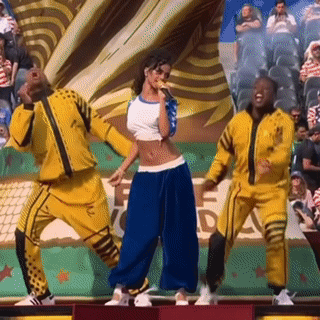 A Woman Is Singing Into A Microphone While Two Men Are Dancing In Front Of A Crowd GIF