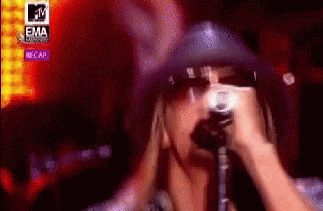A Woman Is Singing Into A Microphone While Wearing A Cowboy Hat And Sunglasses . GIF